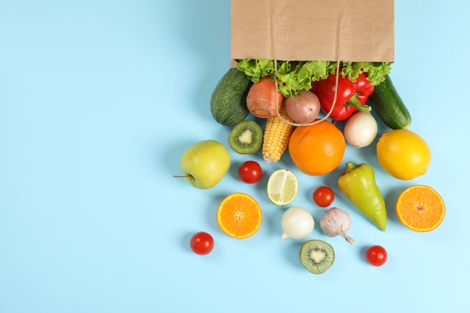 Paper bag, vegetables and fruits on blue background, space for text