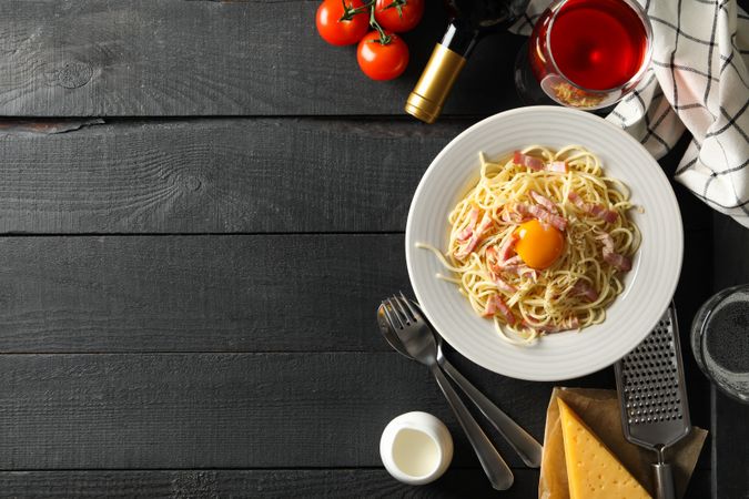 Composition with plate of tasty pasta and ingredients for cooking on wooden background