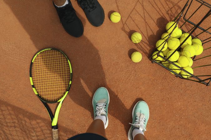 Woman and man legs in sneakers on clay court with tennis balls and racket