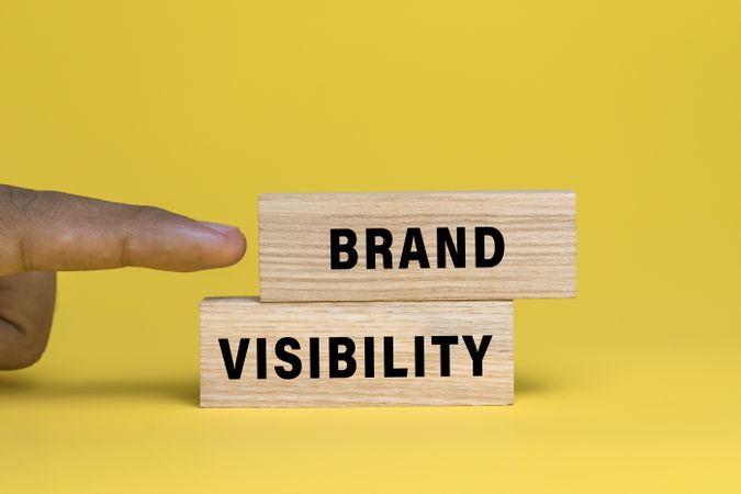 male finger pointing brand visibility words text on wooden blocks isolated on yellow background