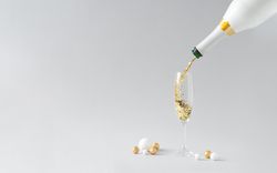 Champagne bottle pouring golden glitter into the glass on light background