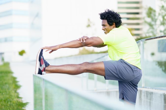 Black man stretching his leg on outdoor railing
