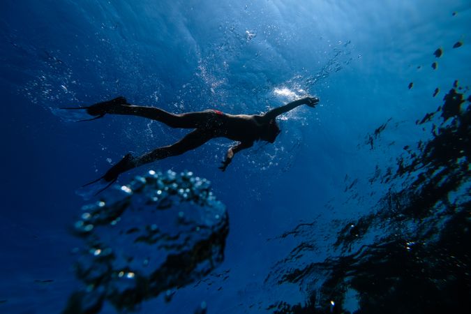 Anonymous male swimmer in diving mask and fins floating underwat
