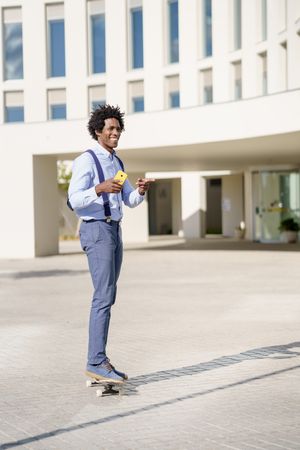 Man pointing to something while on skateboard checking his yellow smart phone