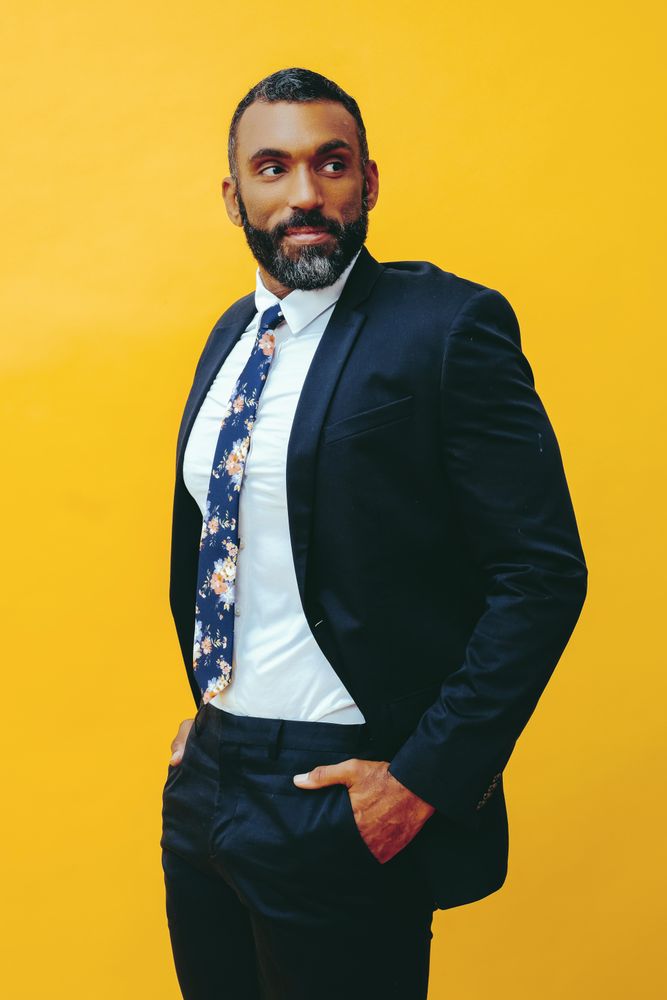 Smiling Black male in navy suit with floral tie in yellow studio