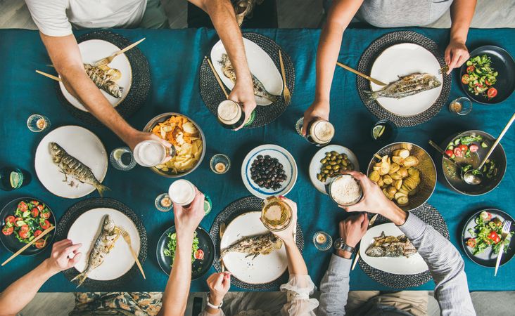 Group of people toasting drinks at table with whole fish plates, side dishes, vertical composition