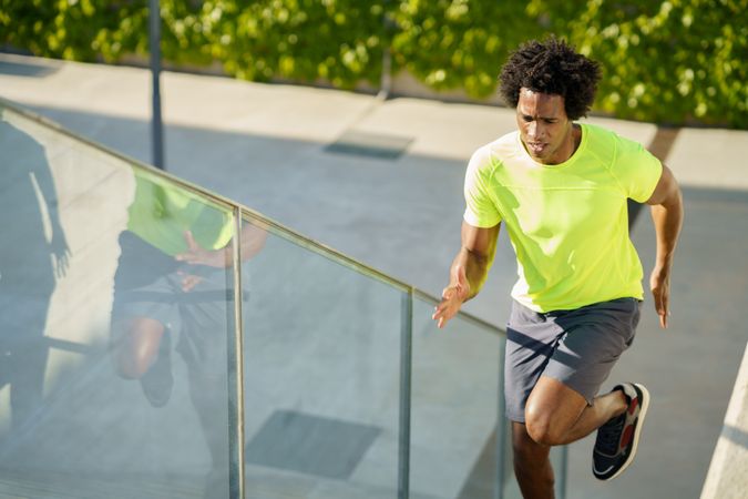 Fit man in neon T-shirt doing cardio on outdoor staircase