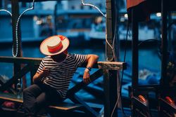 Man in striped shirt with a hat using a phone sitting on a bench outdoor bY7yg5