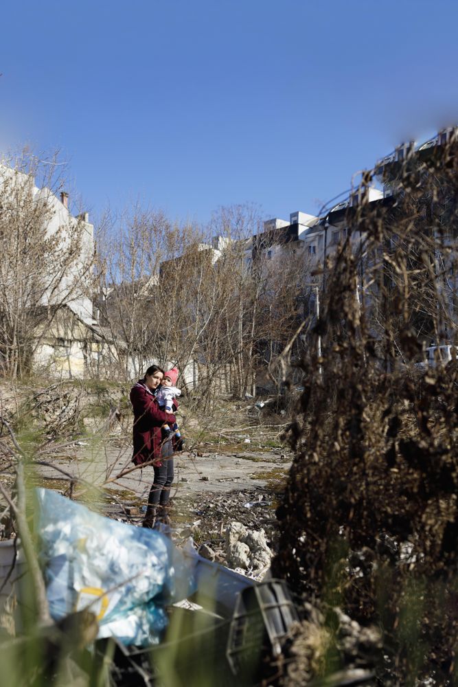 Woman holding her baby in garbage filled clearing, vertical