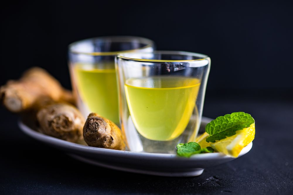 Side view of two yellow detox drinks on silver tray with ginger and lemon