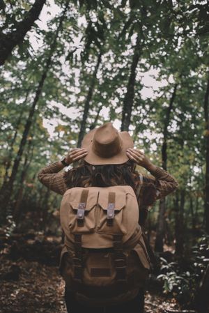 Unrecognizable hiker adjusting hat in green forest