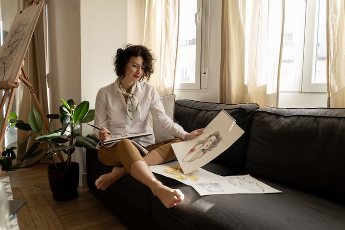 Woman drawing on papers on sofa in room