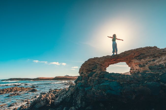Anonymous woman with outstretched arms on cliff near sea