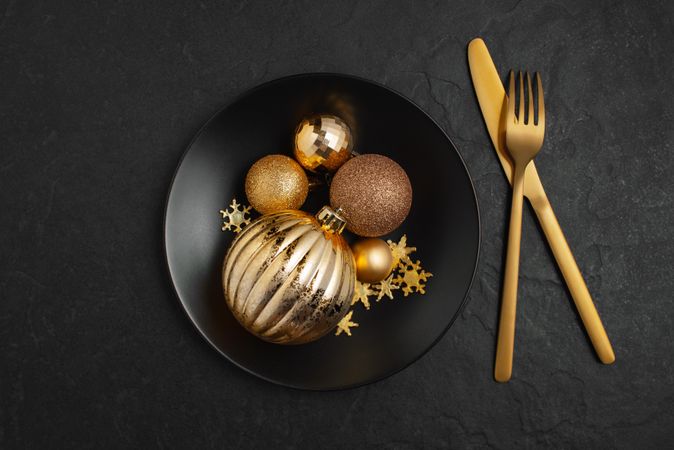 Gold Christmas decorations in dark bowl on table with gold cutlery