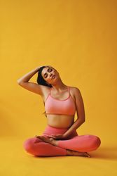 Hispanic female sitting in yoga pose tilting head in yellow studio shoot