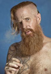 Pensive confident adult red haired hipster lighting cigarette and looking at camera