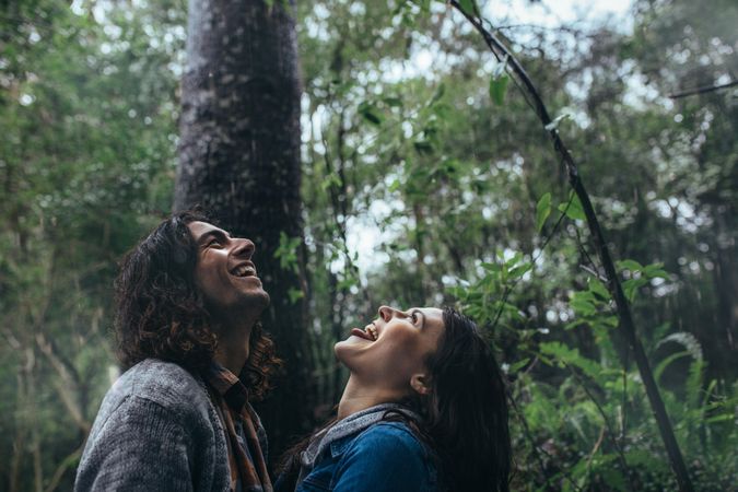 Playful man and woman catching raindrops on tongue in rainforest