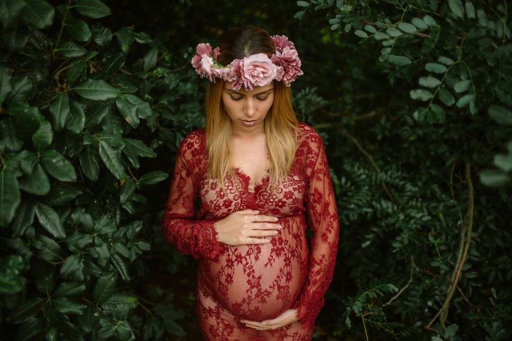 Pregnant woman with closed eyes touching belly and chin while standing in garden in sunny day