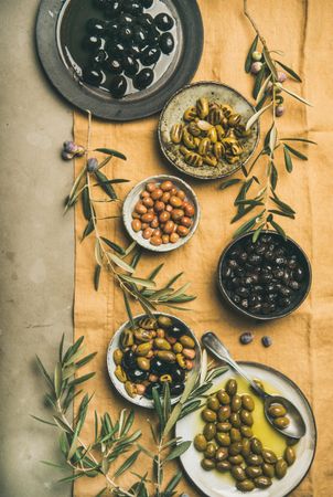 Olives in bowls with branches, on beige table linen, vertical composition