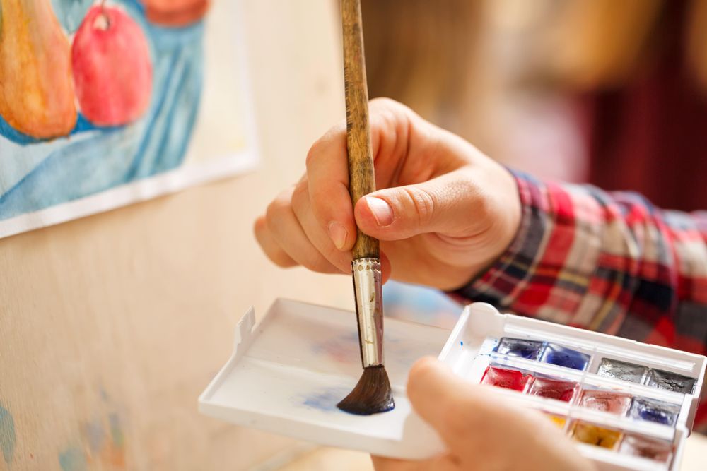 Hand using watercolors in front of an easel