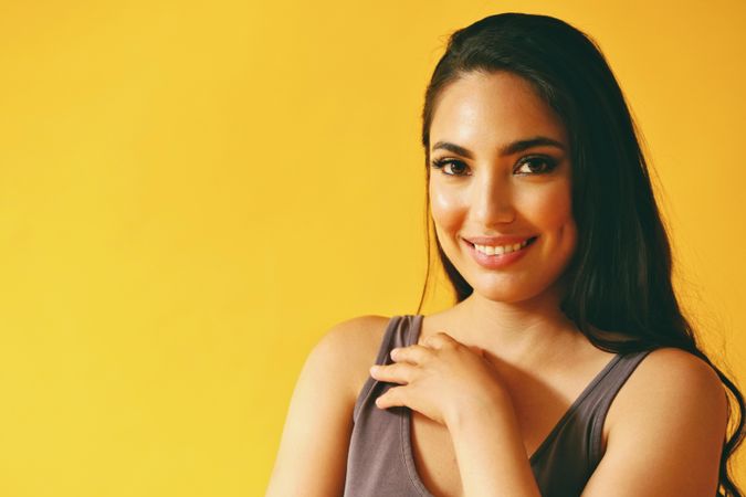 Happy confident Hispanic woman looking at camera in yellow room with her hand to her chest
