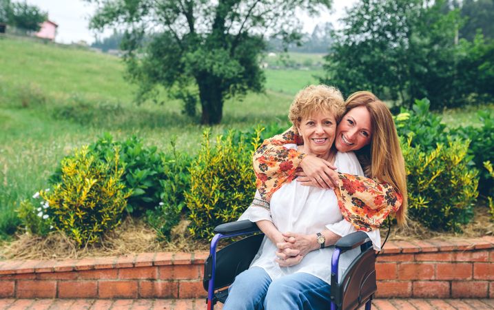 Daughter embracing her mature mother in wheelchair