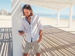 Relaxed man using smartphone in gazebo on beach