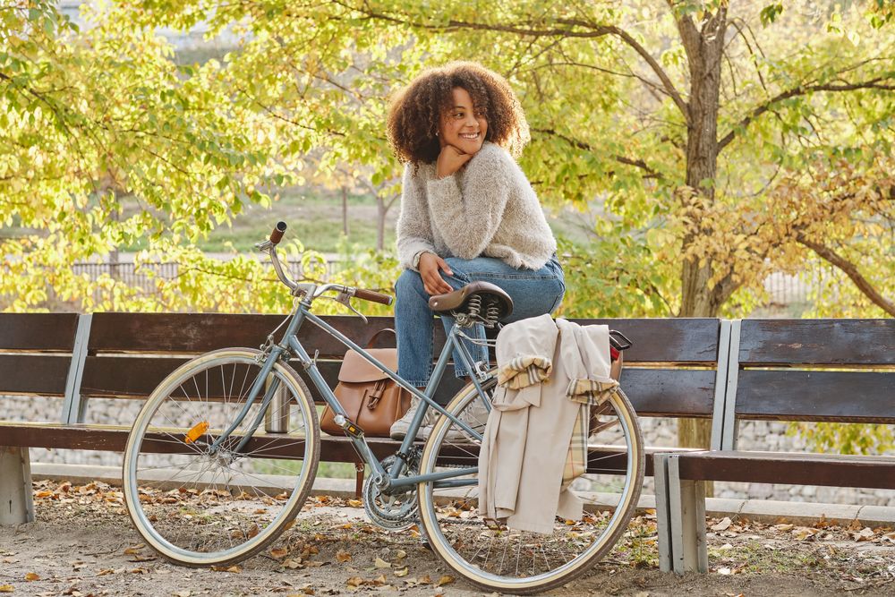 Smiling Black Latina woman sitting on bench near bicycle in park