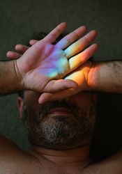 Bearded man covering eyes from rainbow glare