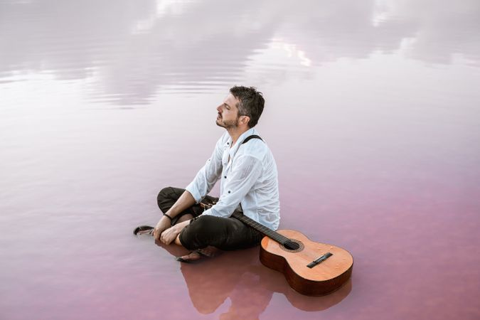 Musician with guitar on pink sandy water