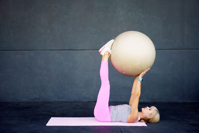 Flexible woman doing pilates exercise with fitness ball in gym on mat