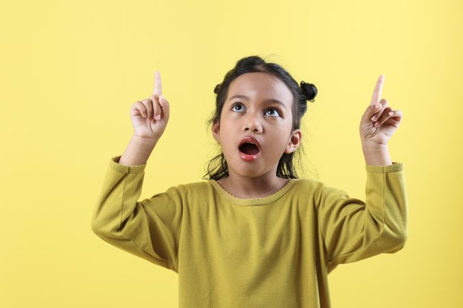 Positive Asian Little Girl Points Above Show Place for Advertising Text Surprised