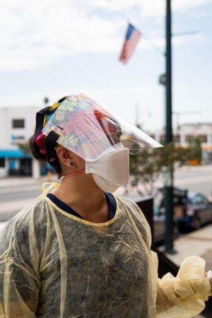 Portrait of nurse in face shield, N95 mask and disposable gown outside with USA flag behind