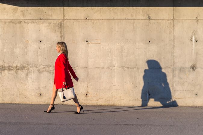 Businesswoman wearing red jacket walking on the street with shadow