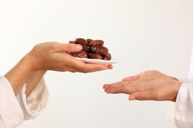 Female Muslim Hand Over A Plate of Dates Fruit Kurma to Other.