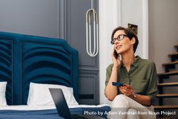 Woman sitting on hotel room bed with phone, laptop and credit card bGB724