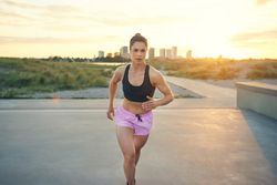 Fit woman jogging with city buildings in background under bright sunlight