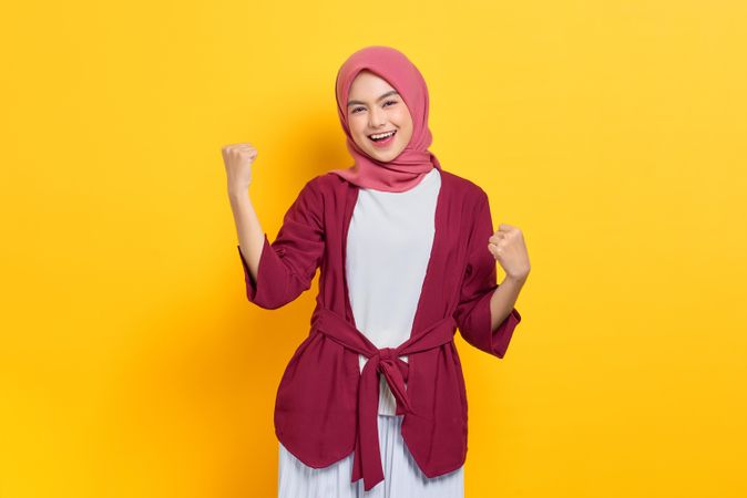 Woman in red headscarf with both arms up in victory