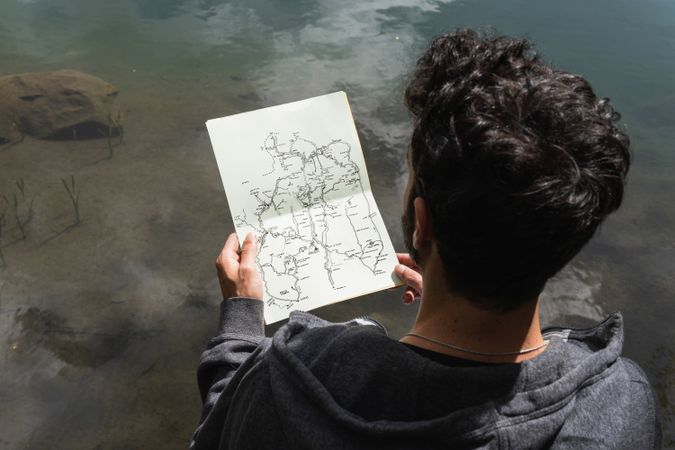 Traveling man reading map near lake in highlands