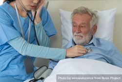 Asian nurse using stethoscope checking on heartbeat examining of older man 5XlyM5