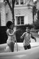 Grayscale photo of a girl and a boy playing with water inside an inflatable swimming pool 0VJE30