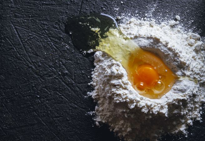 Broken egg and flour on dark background