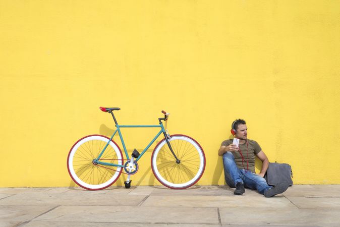 Male sitting in front of yellow wall with bike listening to music