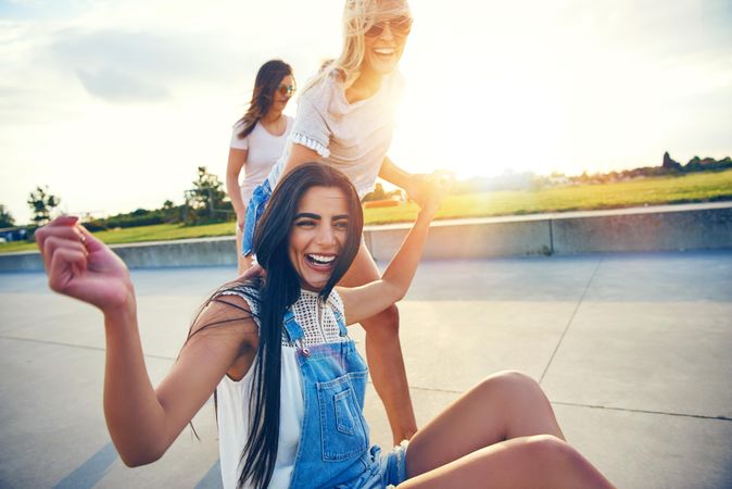 Multi-ethnic female friends helping each other from after falling from skateboarding
