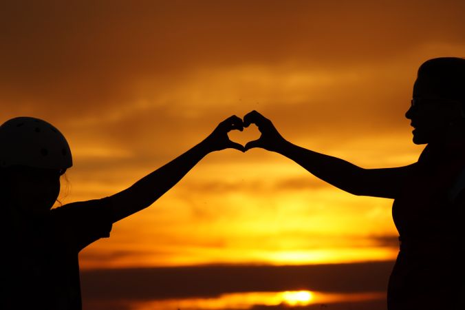 Silhouette of two people making heart shape with their hands during sunset