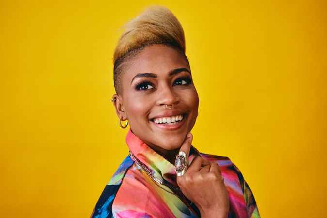 Studio shot of happy Black woman in bright 80s windbreaker jacket looking away with her hand on chin