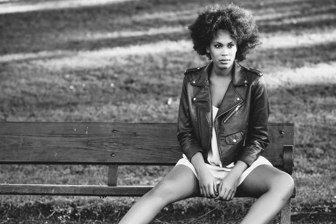 B&W shot of woman sitting outside in red leather jacket on sunny day
