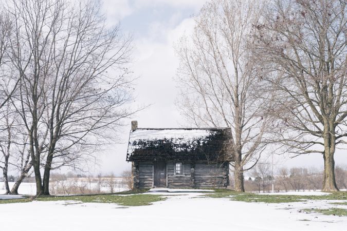 Abandoned log cabin on a snow covered field with some green grass