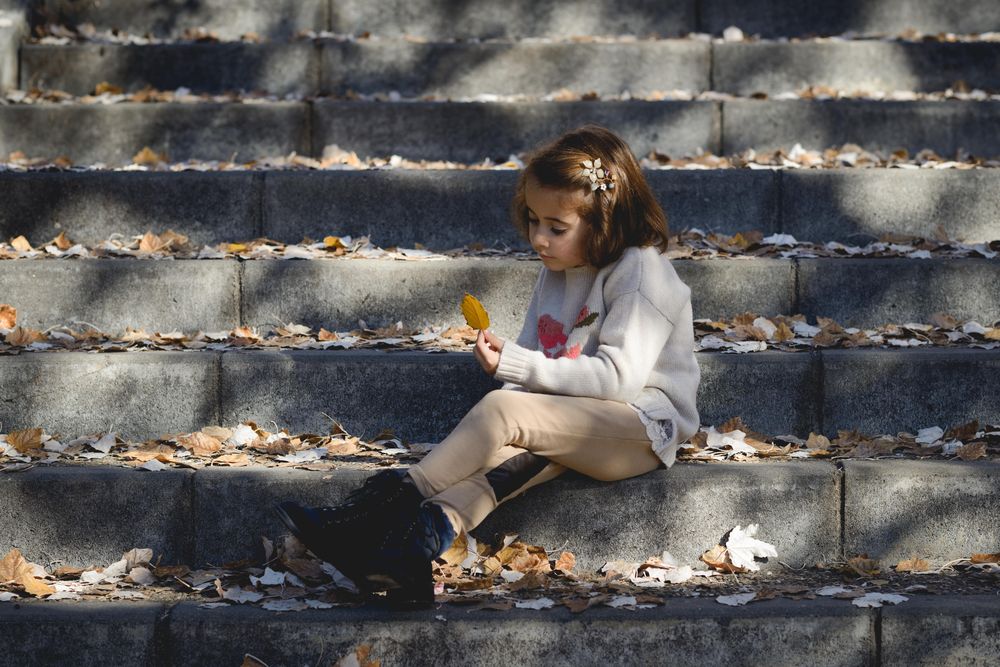 Child sitting on cement steps in outdoor park looking at a autumn leaf