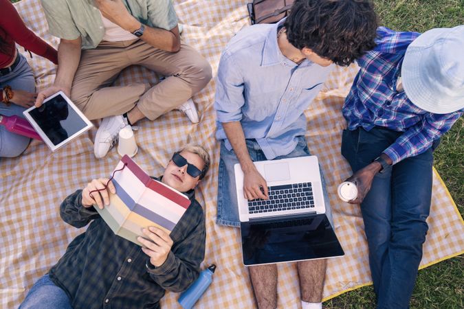 High angle view of diverse students studying together on a picnic blanket outdoors.